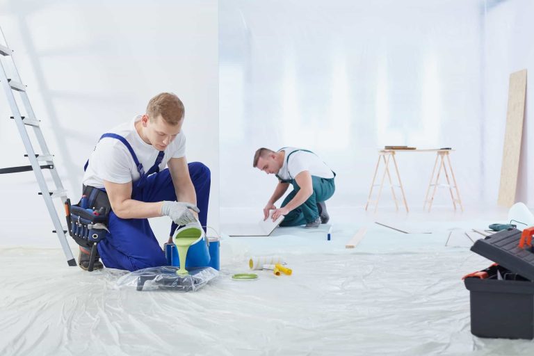 Workers renovating room with green paint and floor tiles, wearing blue overalls