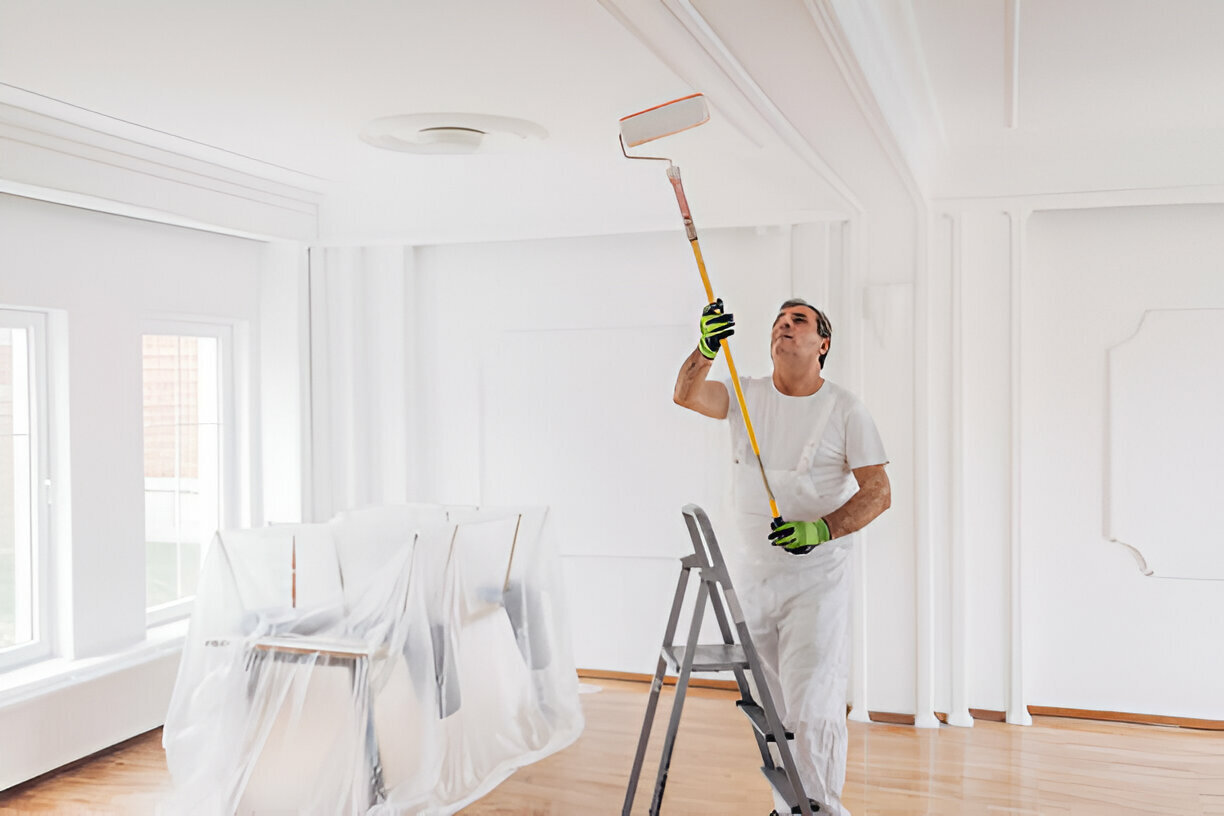 Painter using a roller to paint a white ceiling.